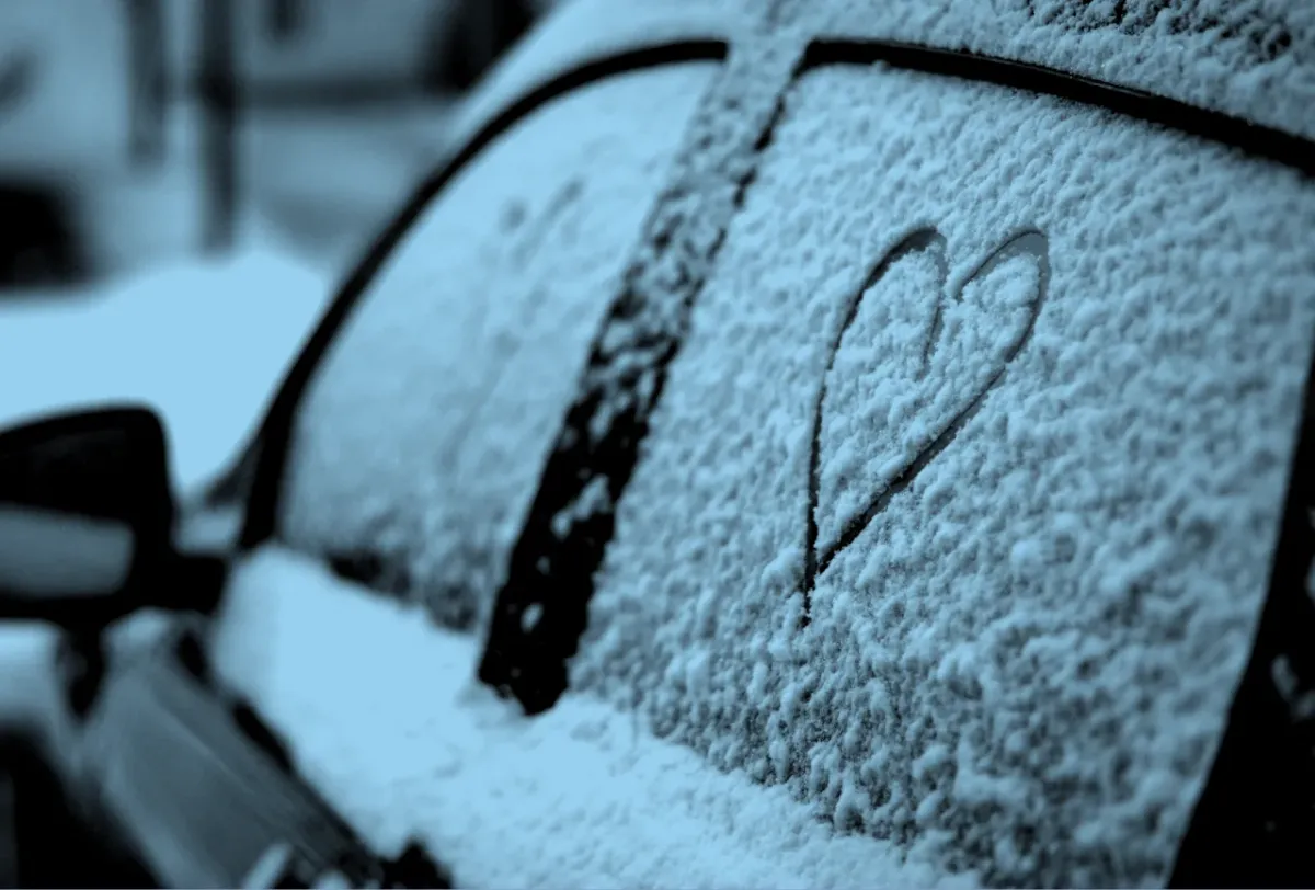 A heart drawn in snow on the window of a car in winter