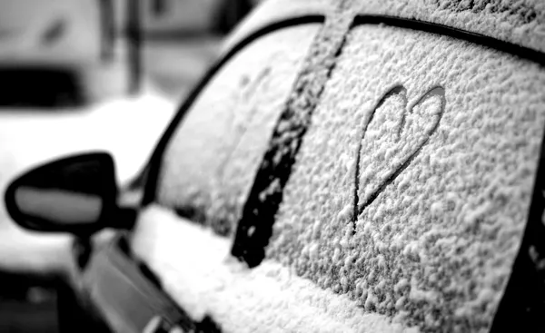 A heart drawn in snow on the window of a car in winter