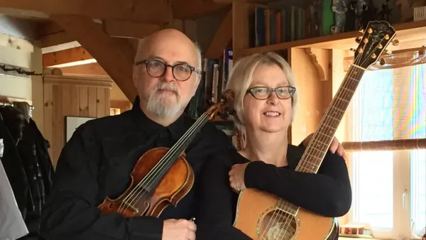 Two sixty-something musicians standing side by side with their instruments, a fiddle and guitar