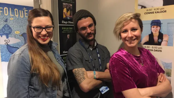 Québec trad trio Été standing in front of posters outside the Folquébec showcase (hotel) room at Folk Alliance 2019 in Montréal.